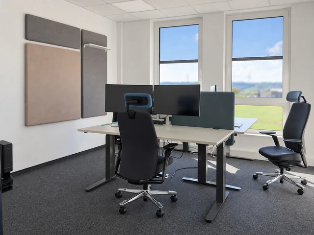 Heller Arbeitsplatz bei innos mit zwei Monitoren, höhenverstellbaren Schreibtischen und Akustikelementen.